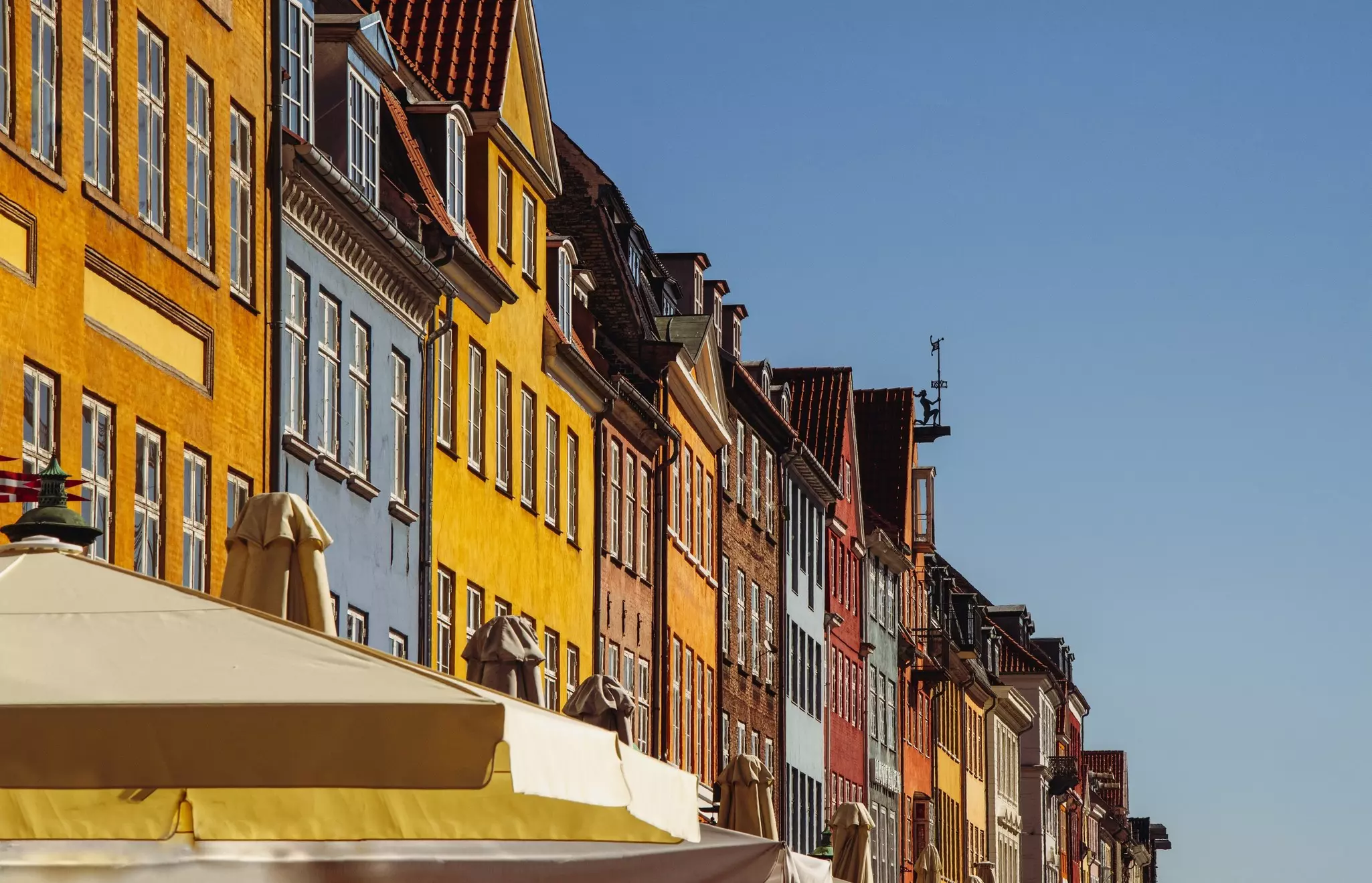 Upper part of colorful townhouses in a row with cafes sunshades in the historic picturesque waterfront district of Nyhavn, Copenhagen.