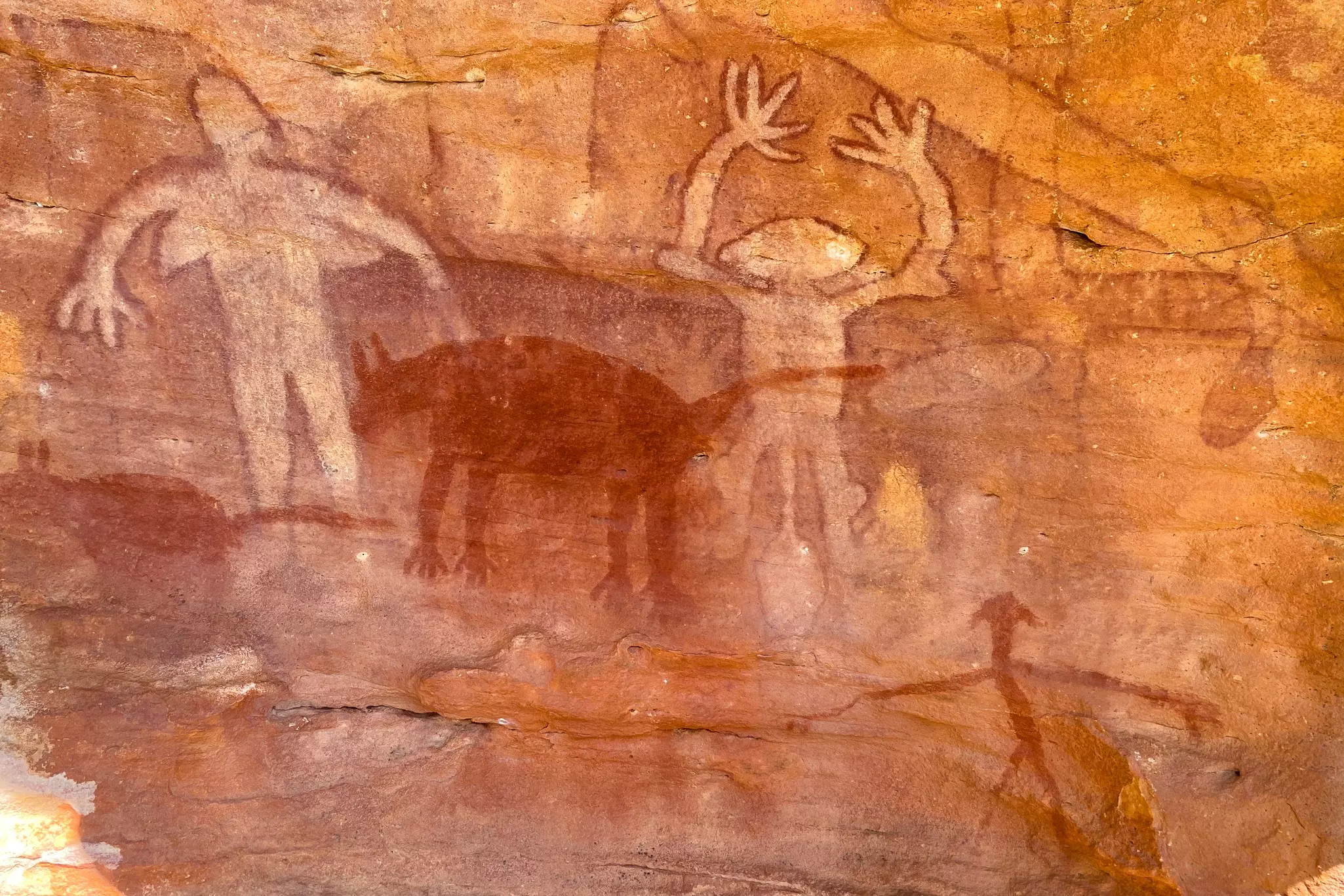 Figures and a four-legged creature painted on a red rock face.