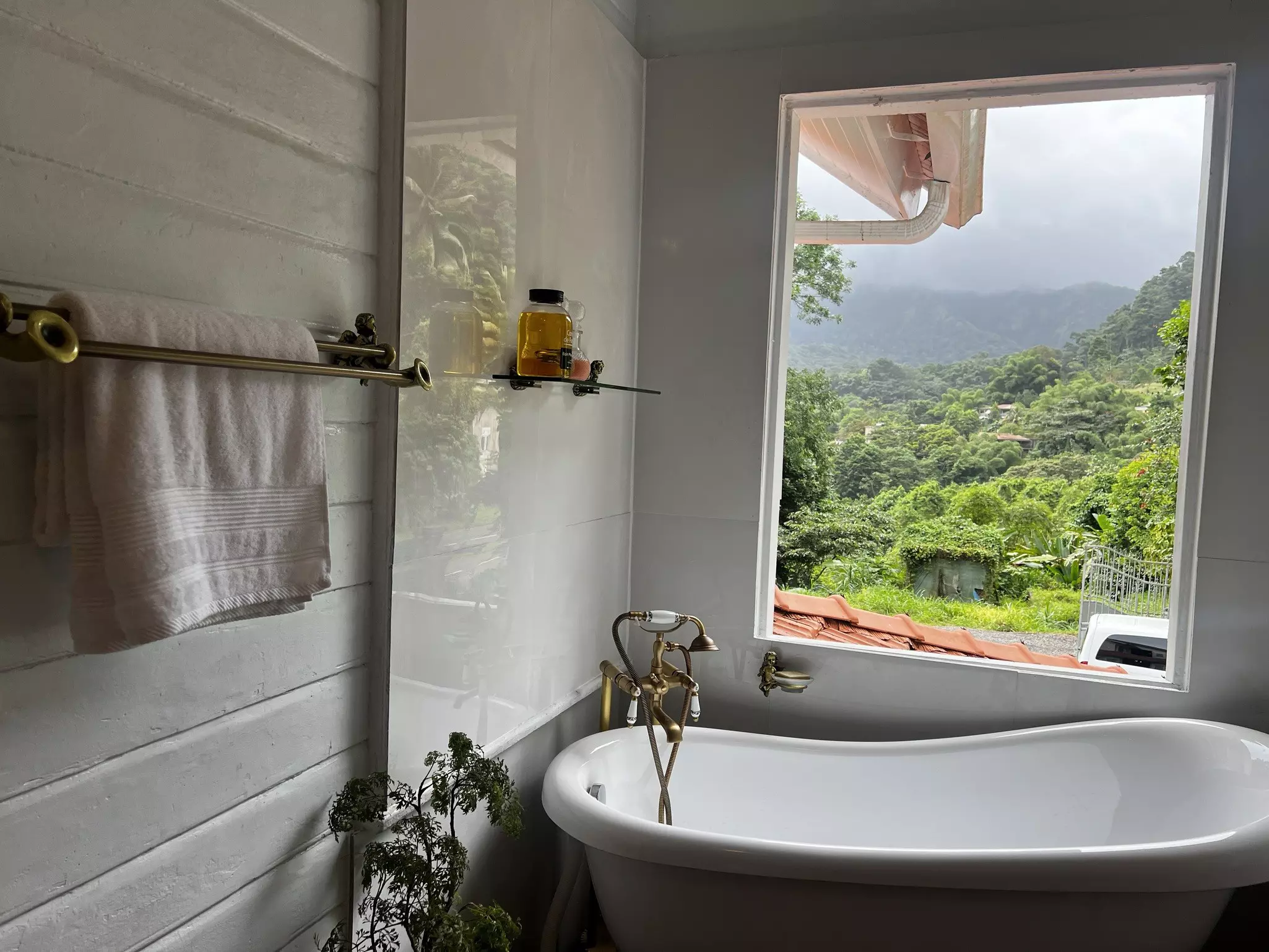 A clawfoot bathtub sits in front of a large window with incredible views of a lush hilly landscape.