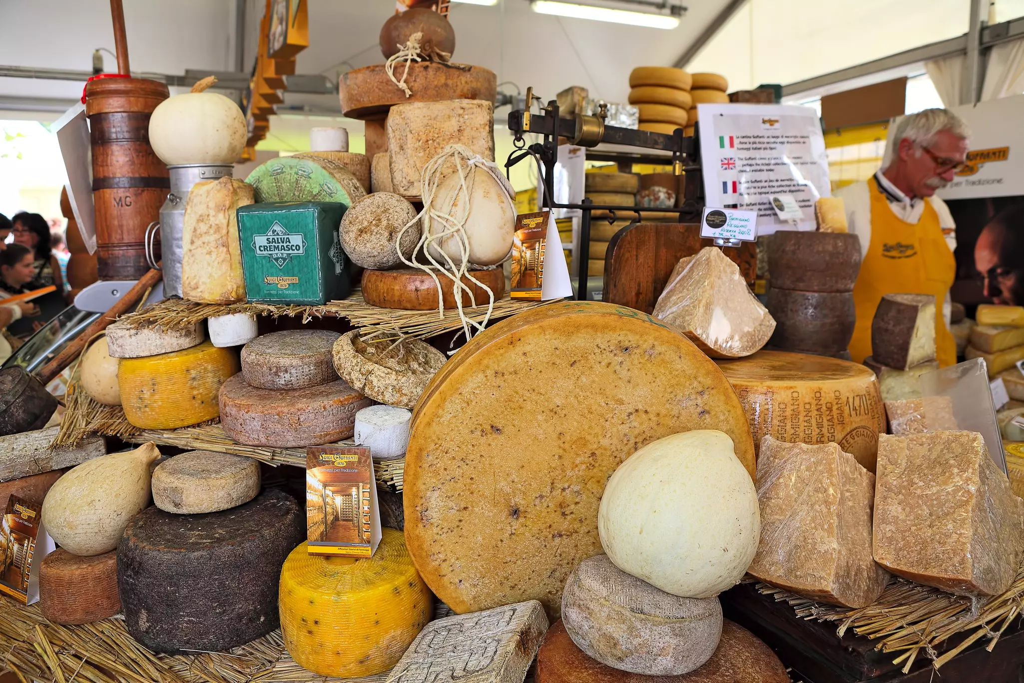 Wheels of cheese are piled high at a stall at a market.