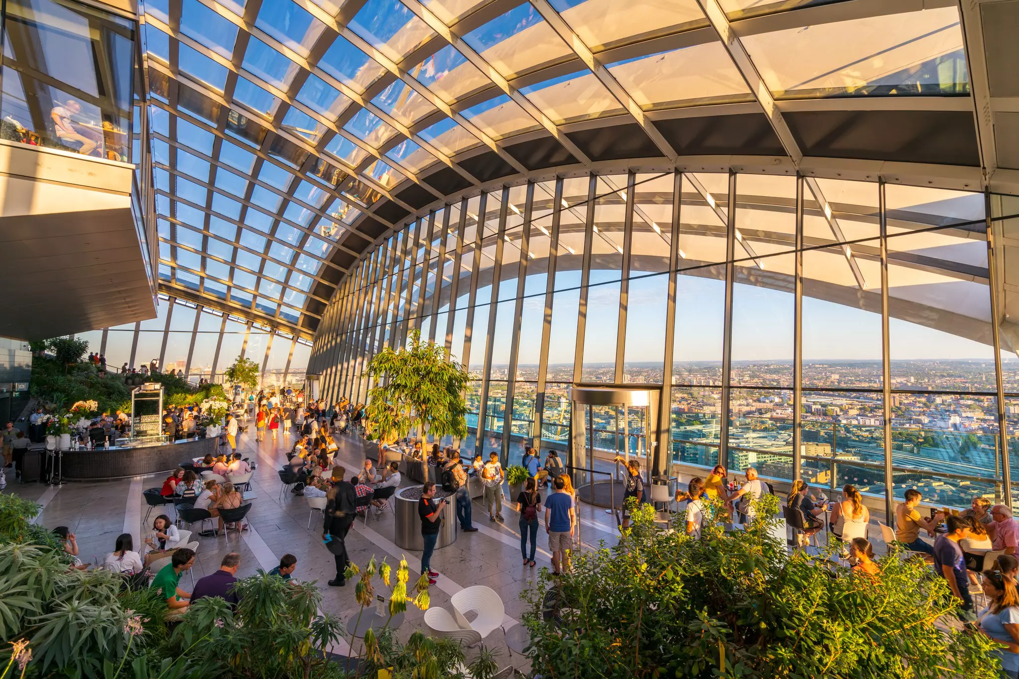 People in an indoor garden in a large glass atrium with views of the city spreading into the distance.