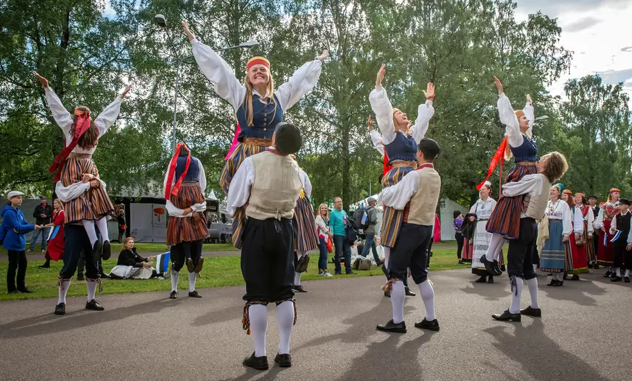 Estonian folk dancers in traditional clothing perform outdoors.