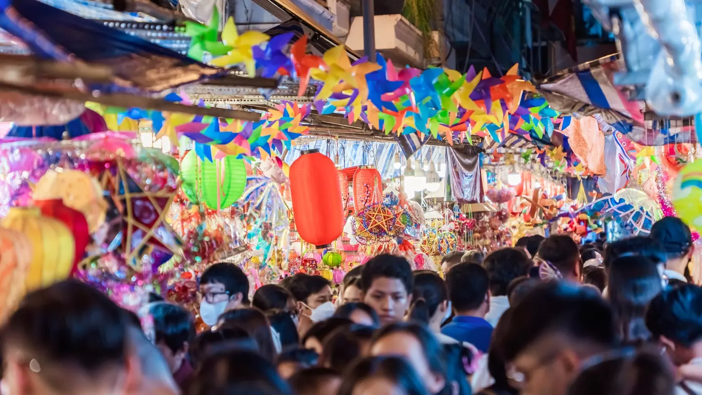 A very busy street with many shoppers. Stalls display colourful lanterns for sale.
