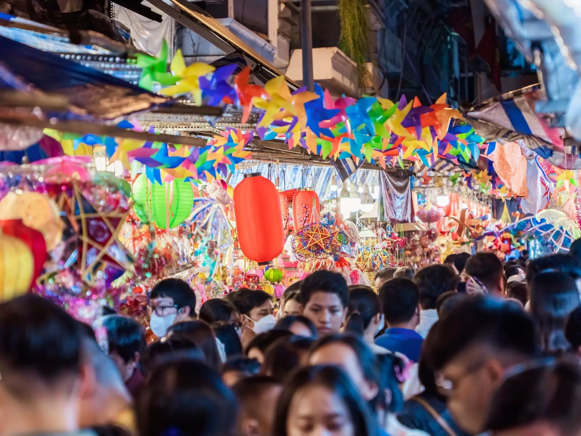 A very busy street with many shoppers. Stalls display colourful lanterns for sale.