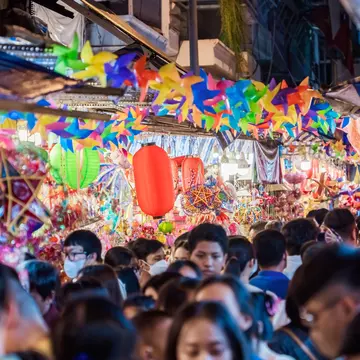 A very busy street with many shoppers. Stalls display colourful lanterns for sale.