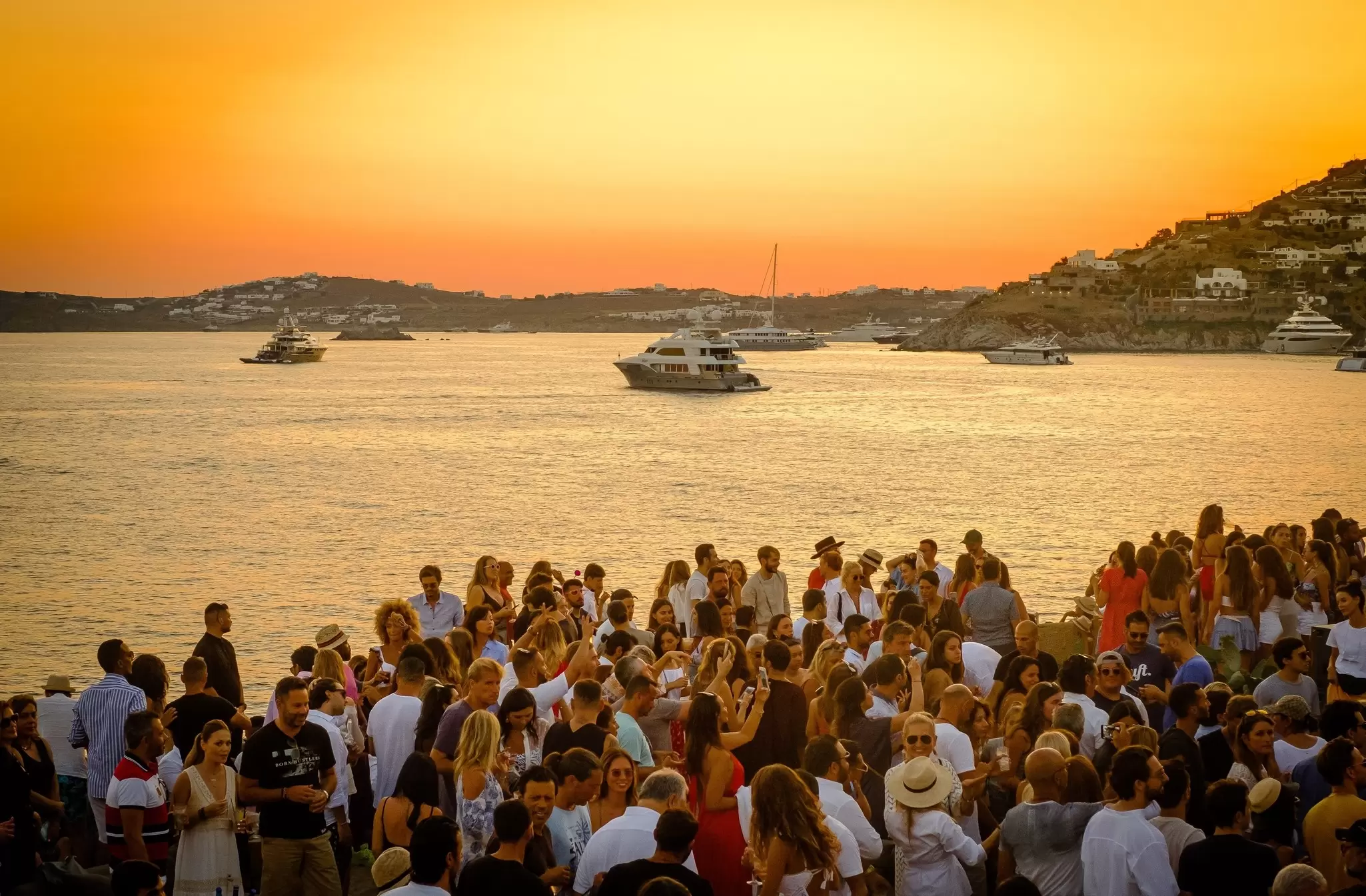 People at a summer beach party at sunset in Mykonos, Greece. 