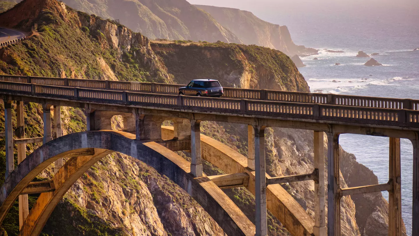 A car drives on a bridge over a ravine by the coast at sunset.
