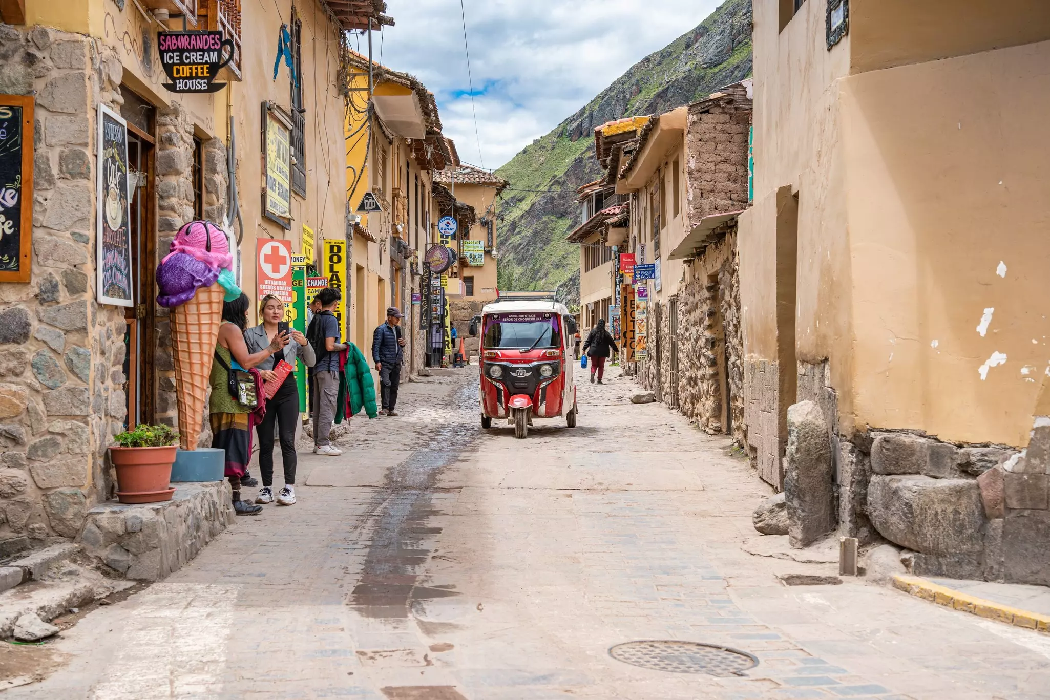 A three-wheeled taxi is pictured on a narrow cobblestone street in a town.