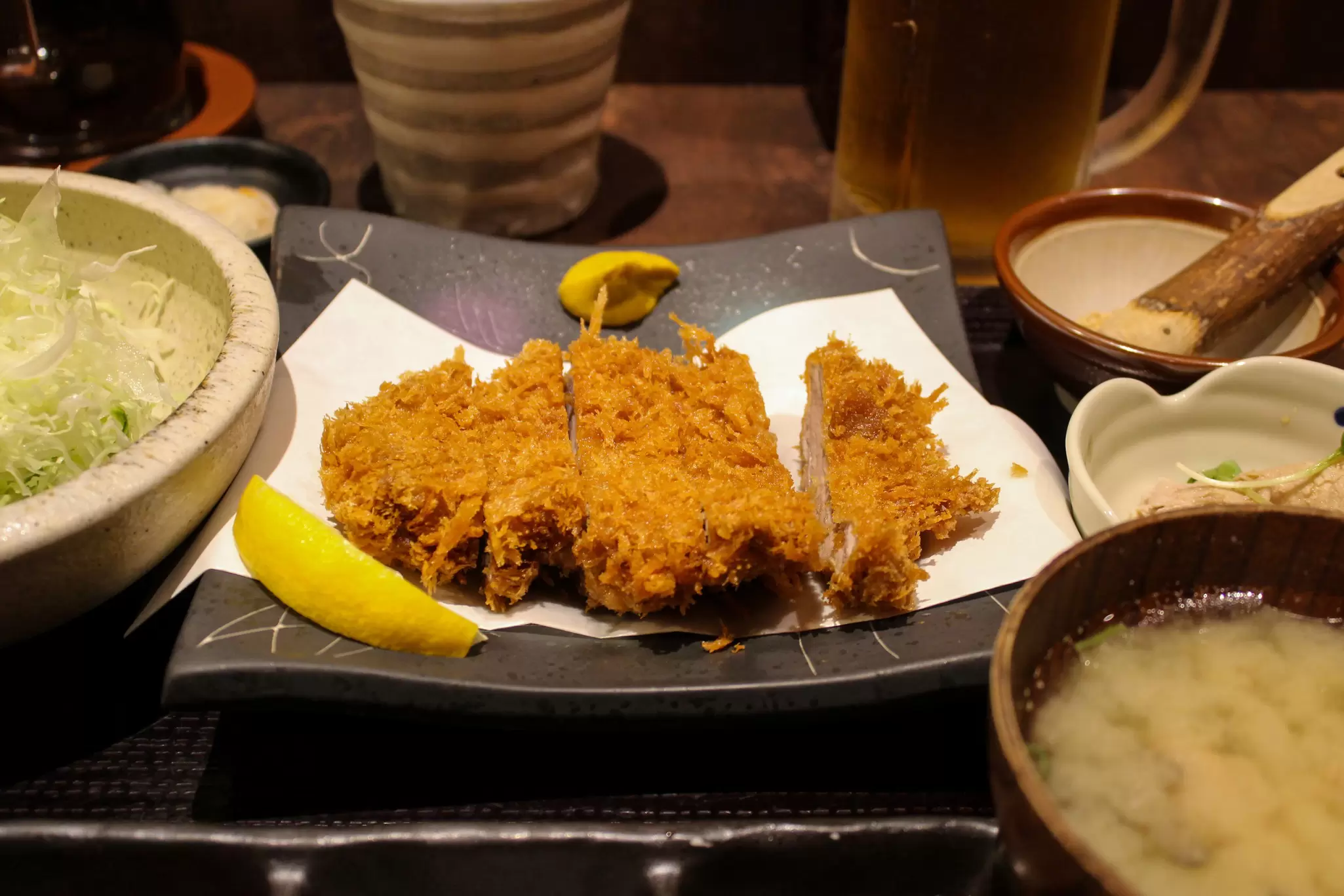 A sliced fried pork cutlet on a white napkin on a plate with other dishes on the side.