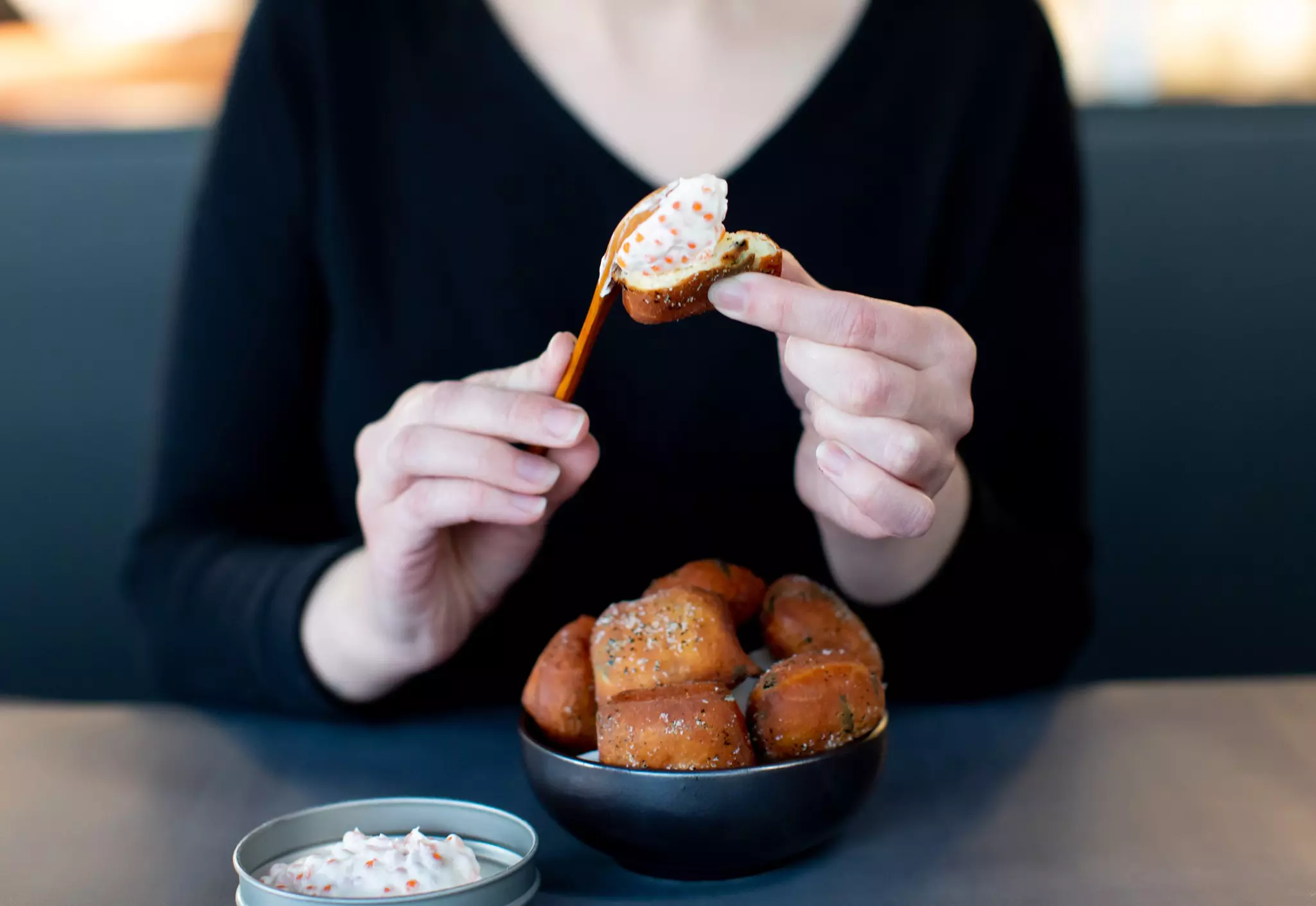 A woman puts a creamy sauce on donuts at a fine-dining restaurant.
