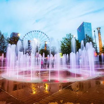 Fountains in the shape of the Olympic Rings shoot water upwards at Centennial Olympic Park at dusk