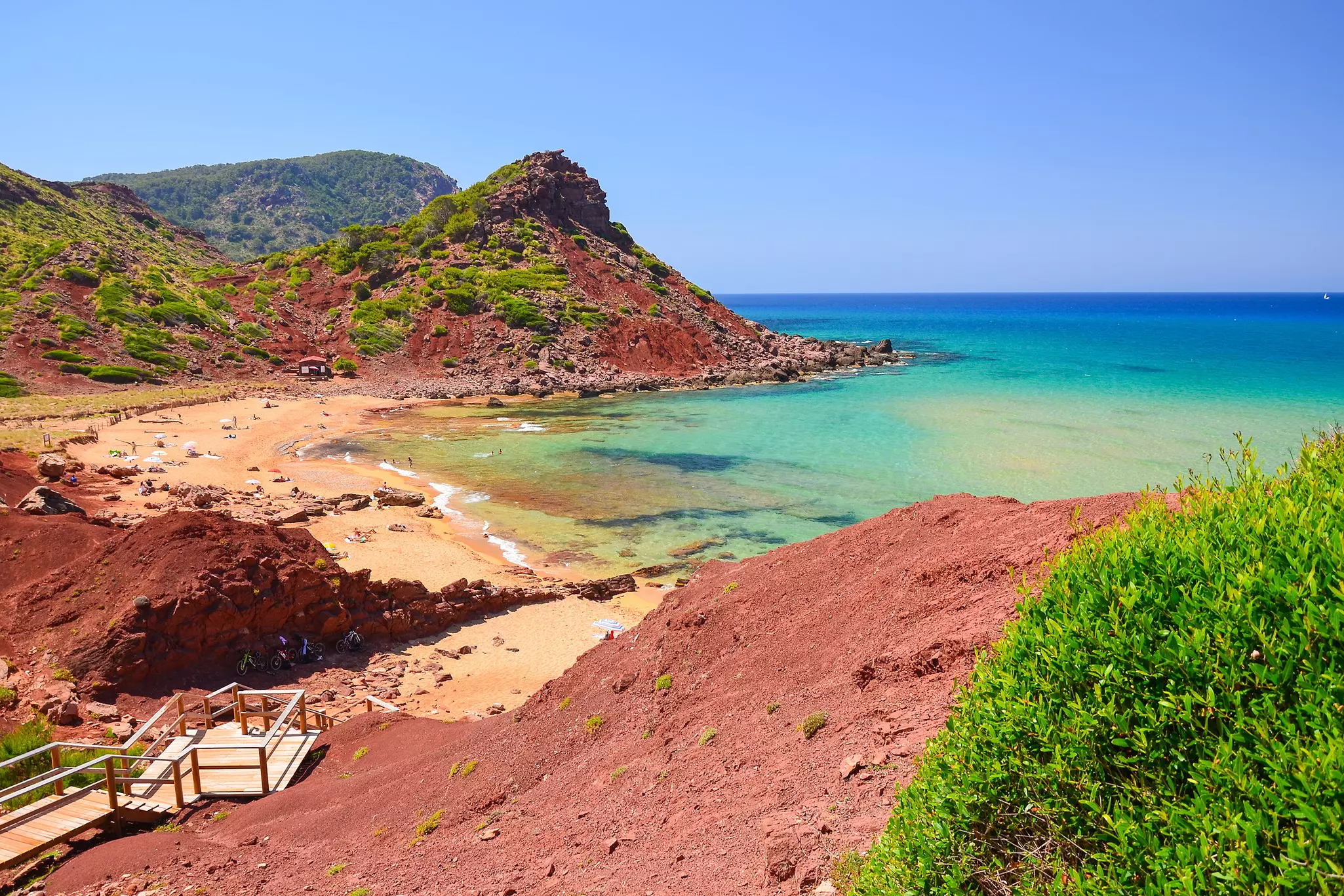 Wooden steps leading to a beach with gold and reddish sand.