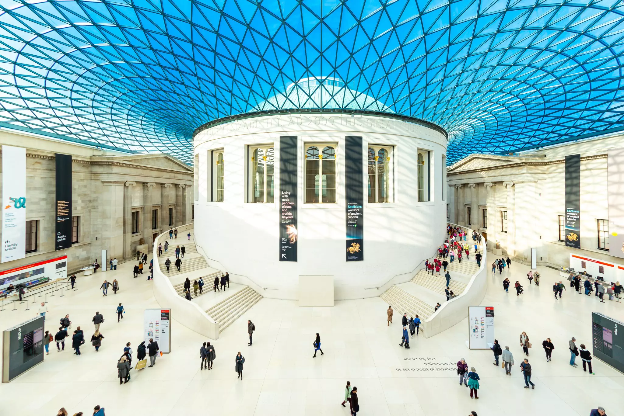 People move around a large central rotunda in a space with a glass roof