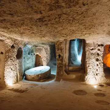 Low rock-cut chamber with a large round millstone door beside dim doorways leading to deeper tunnels