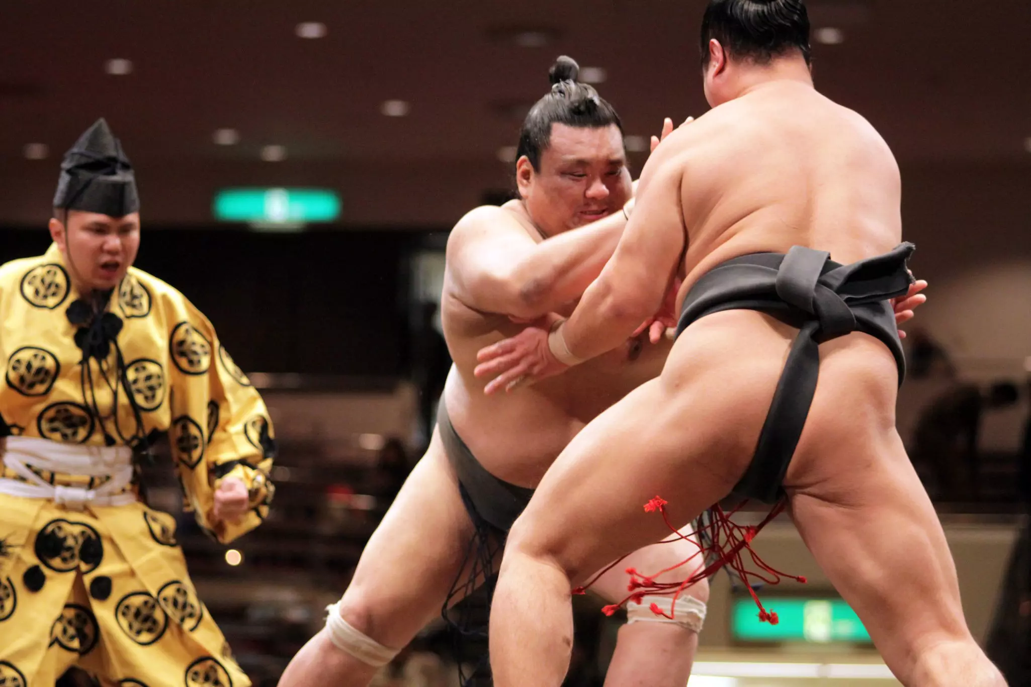 Two sumo wrestlers fight with each other in the ring as the umpire looks on.