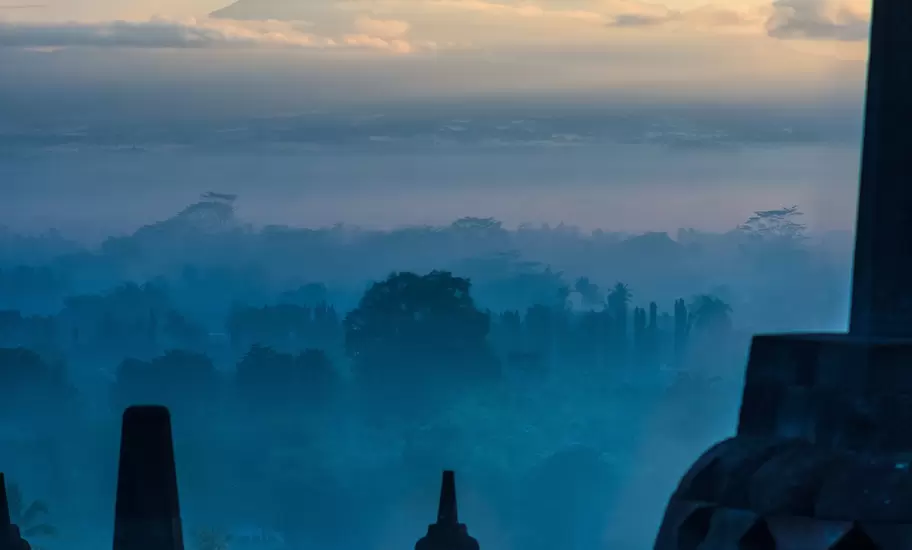 Yogyakarta region: Borobudur stupas silhouetted at dawn, with misty forest and Mt Merapi's cone beyond