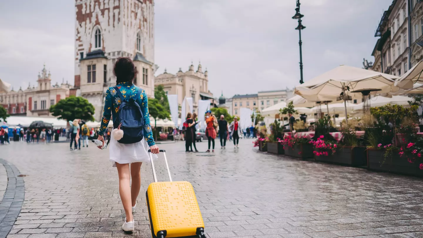 A woman walking through a medieval square in Kraków with a suitcase