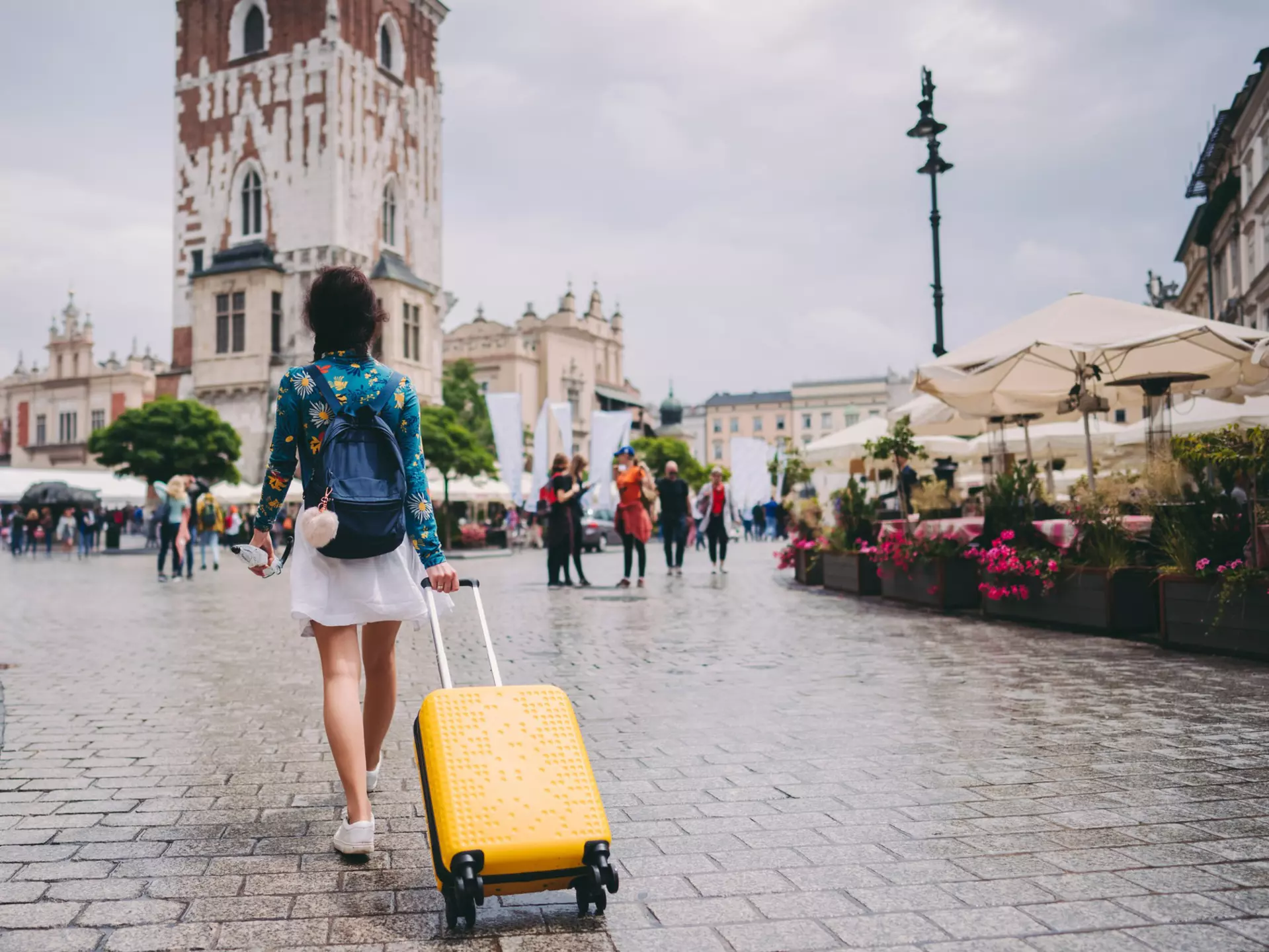 A woman walking through a medieval square in Kraków with a suitcase