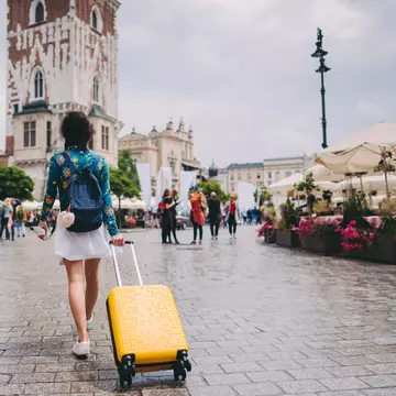 A woman walking through a medieval square in Kraków with a suitcase