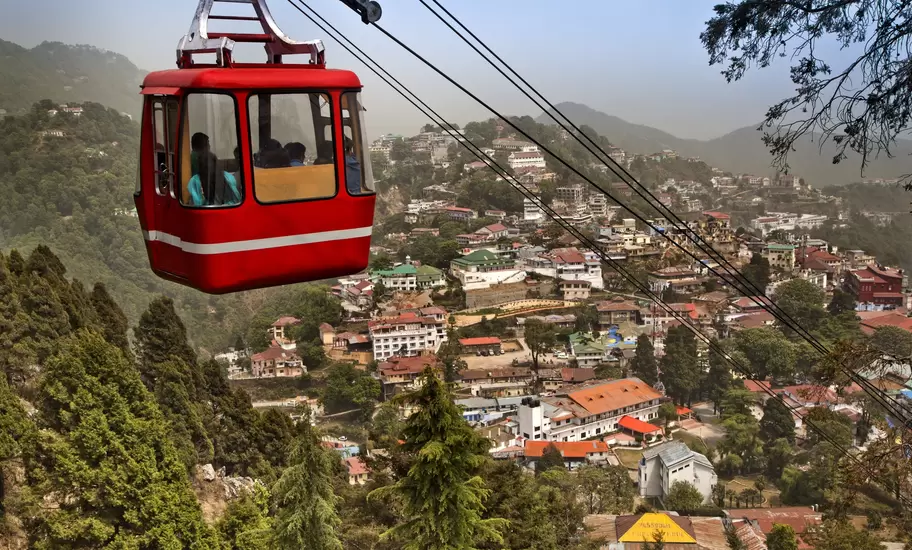 Mussoorie, India: red cable car on a ropeway above a hillside town of red-roofed buildings among deodar trees