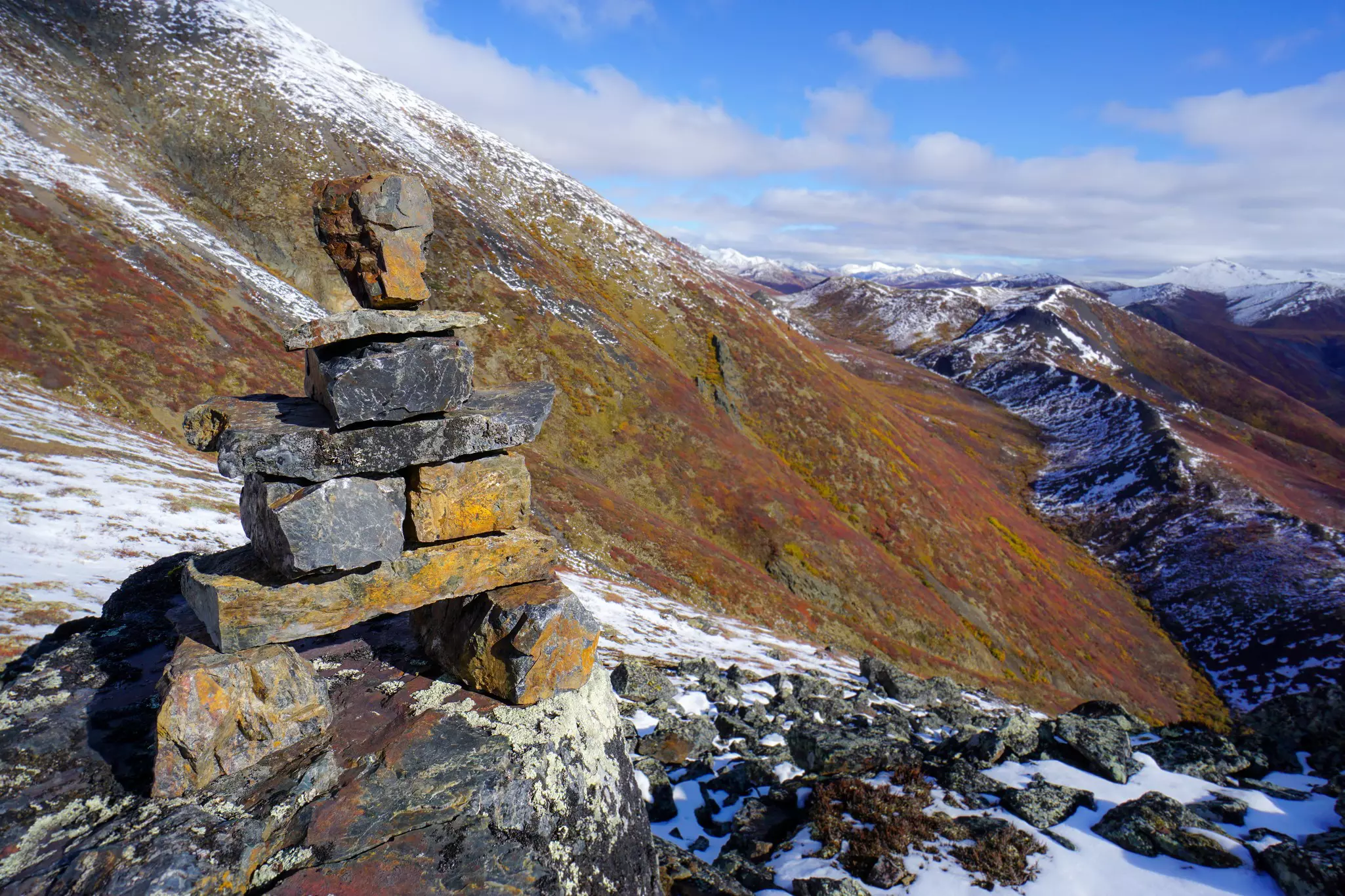 An inukshuk (cairn) on a rocky hillside with snow.