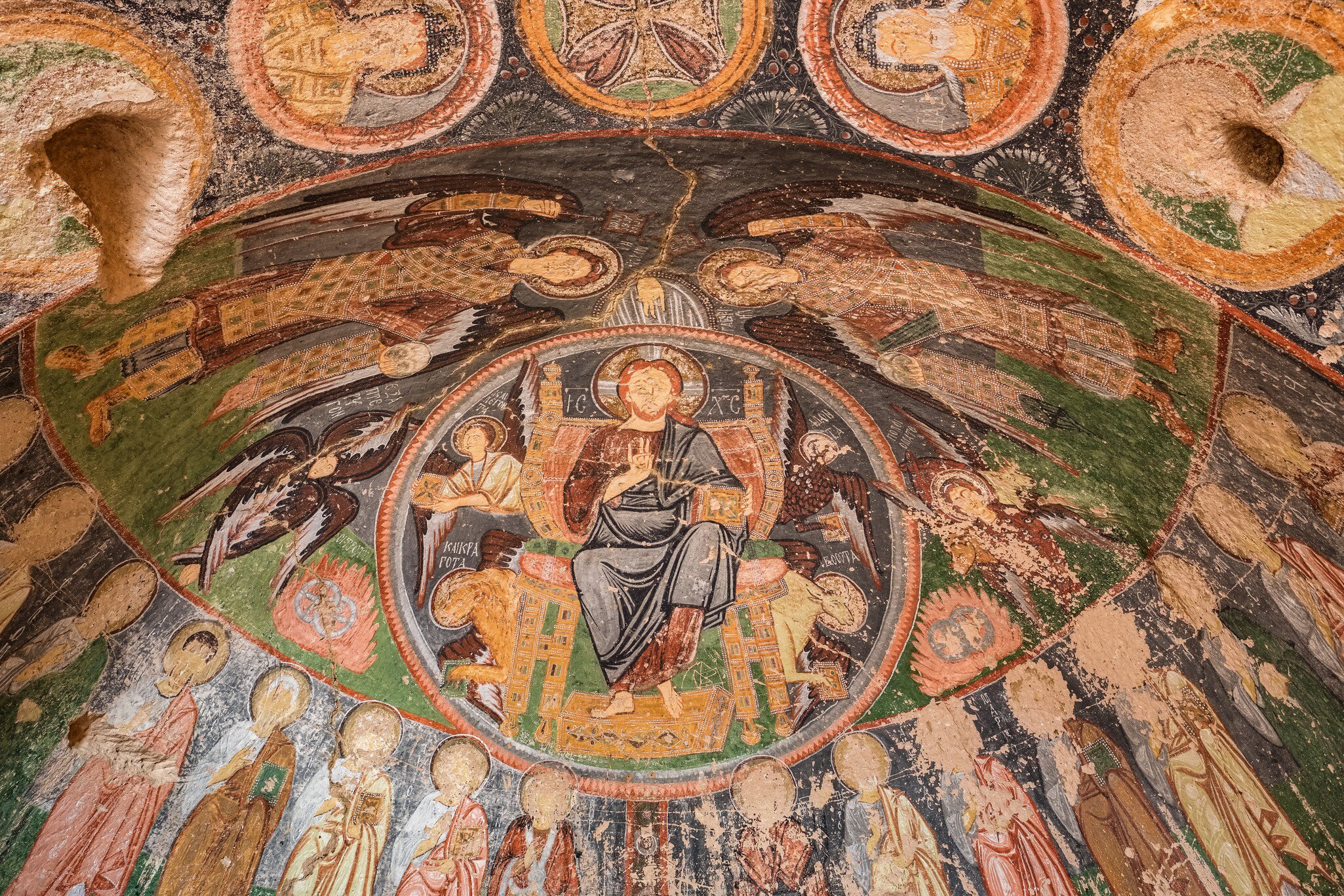 Painted cave ceiling with a haloed seated figure in a circle, winged angels around it and a row of saints below