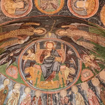 Painted cave ceiling with a haloed seated figure in a circle, winged angels around it and a row of saints below