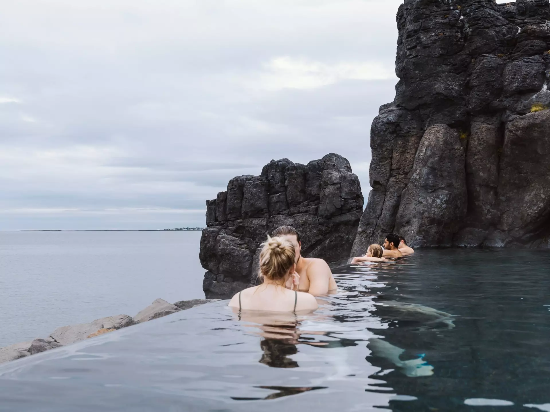 People soak in a heated outdoor pool cut into rock and overlooking the sea.