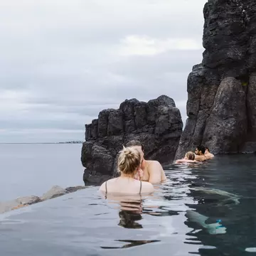 People soak in a heated outdoor pool cut into rock and overlooking the sea.