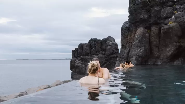 People soak in a heated outdoor pool cut into rock and overlooking the sea.
