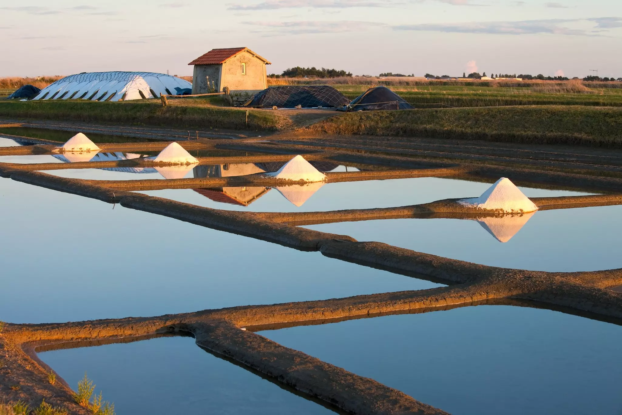 Salt marshes on the island of Noirmoutier in France. The sun rises on ponds, basins and salt piles. 