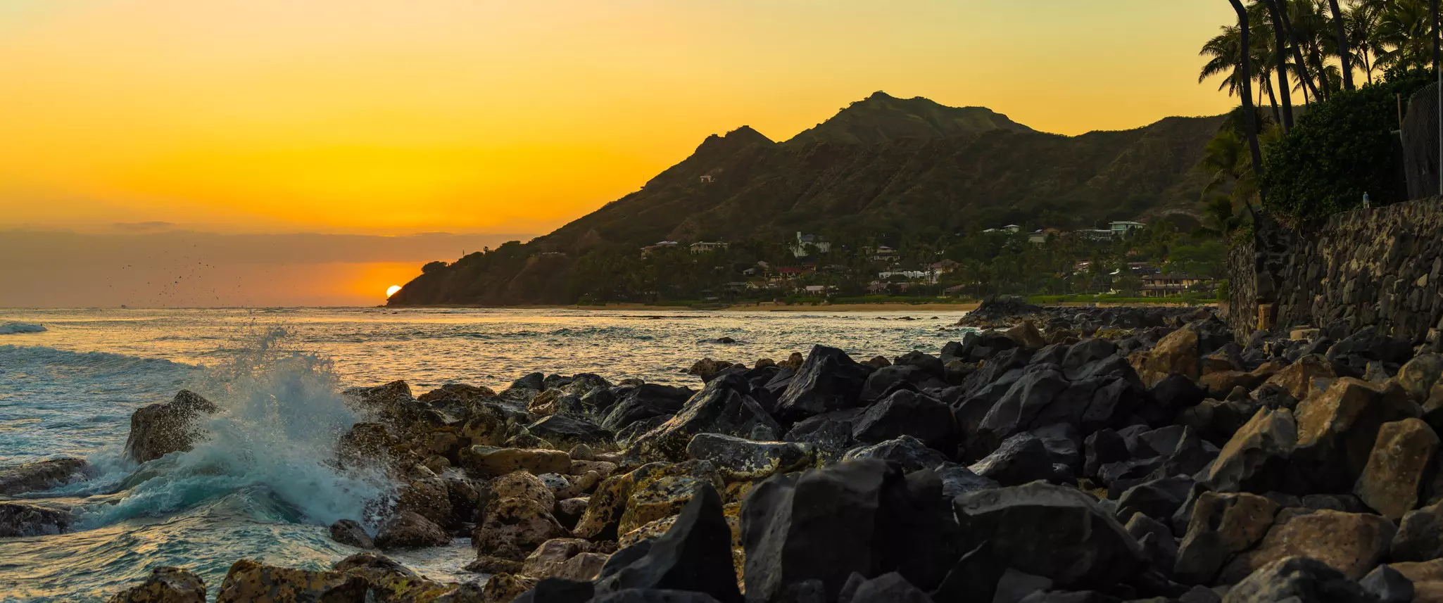 Tropical island panoramic seascape of the iconic volcanic crater landmark, Diamond Head, from Blackpoint in Kahala, Hawaii as the sun is about to disappear behind the mountain and the horizon