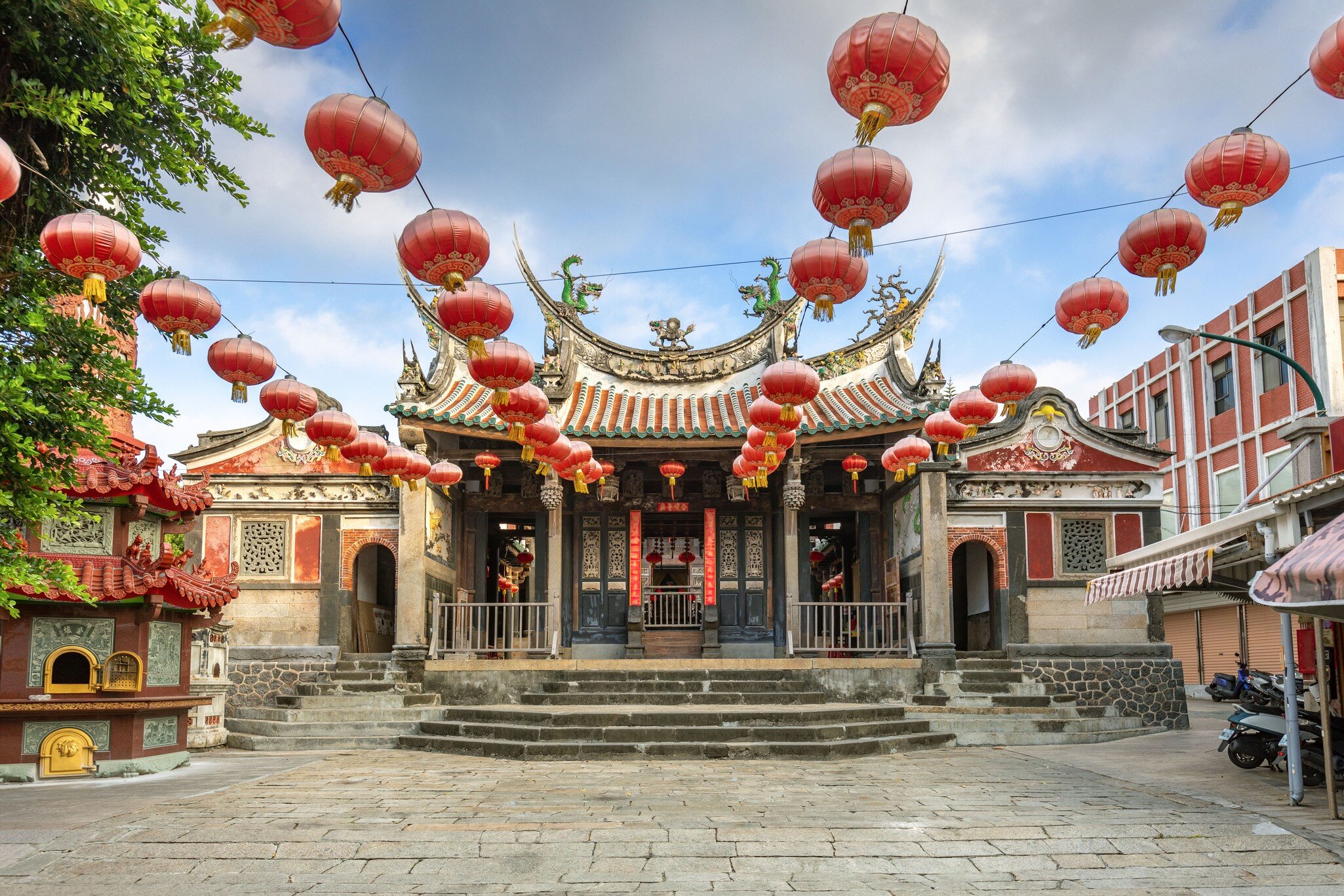 Ornate temple with curved tiled roofs and red paper lanterns overhead in Magong, Penghu, Taiwan, under a blue sky.