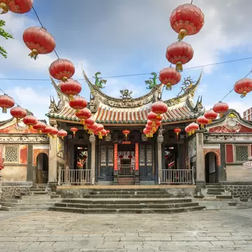 Ornate temple with curved tiled roofs and red paper lanterns overhead in Magong, Penghu, Taiwan, under a blue sky.