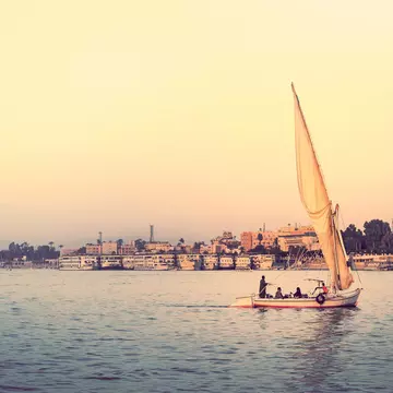 A small sailboat on a wide river at sunset.