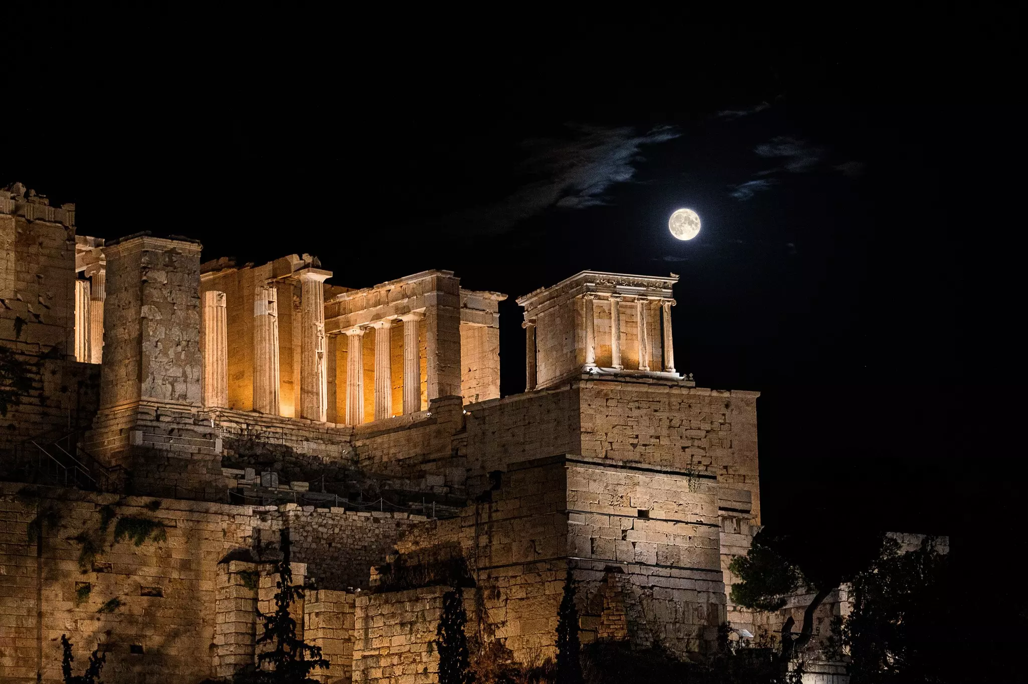 The full moon at night over an ancient structure on a hill.