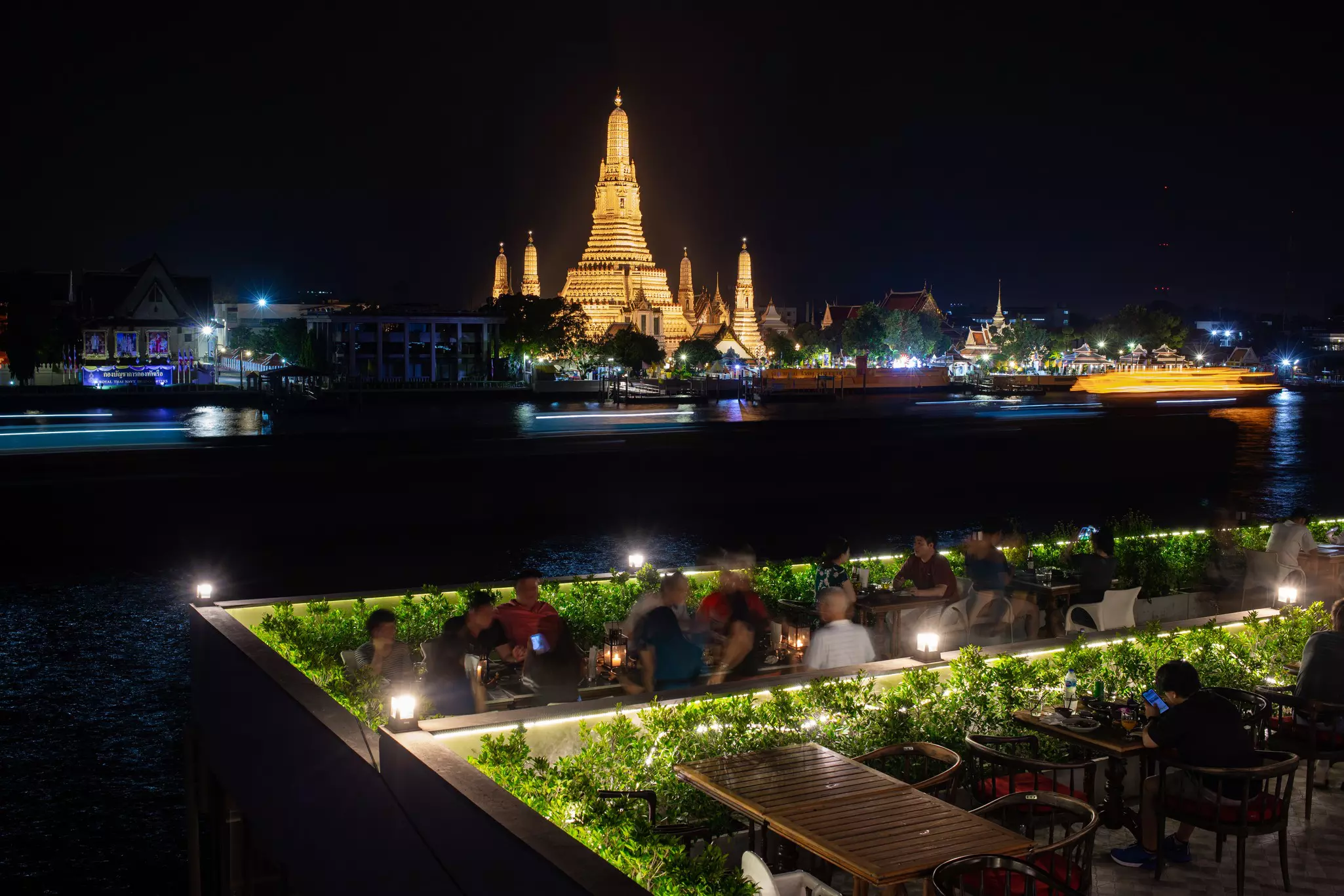 A view of a golden pagoda from the terrace of an outdoor restaurant on a river.