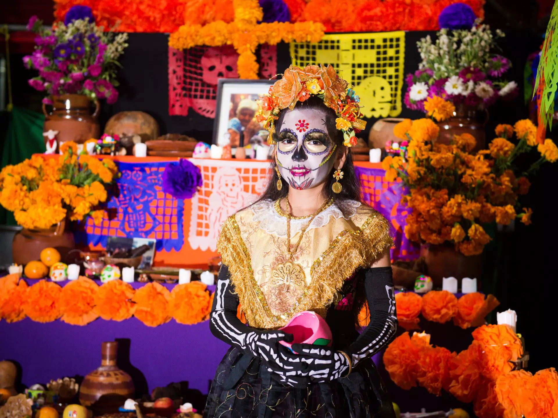 Girl in skeleton costume and face paint stands in front of an altar for the Day of the Dead festival in Mexico