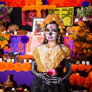 Girl in skeleton costume and face paint stands in front of an altar for the Day of the Dead festival in Mexico