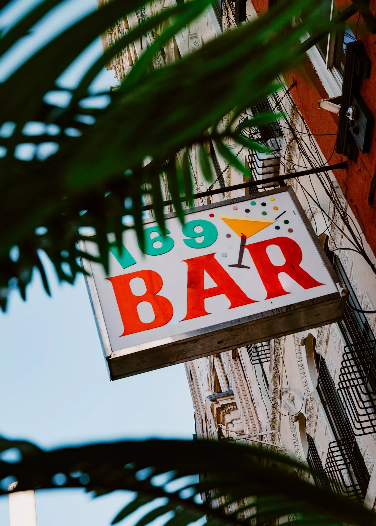 A shot of a neon sign that says 169 Bar bolted to the side of a pinkish building