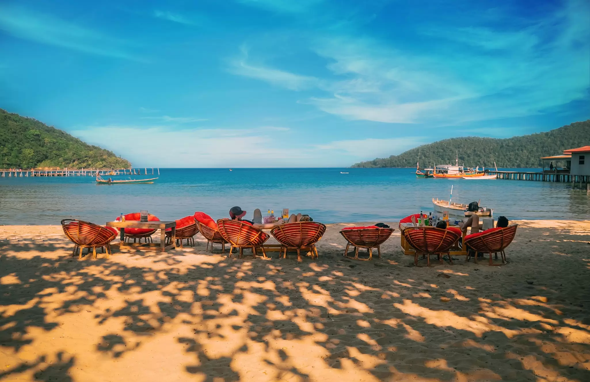 Travelers relaxing in wicker chairs on the sand on Koh Rong Sanloem, Cambodia. 