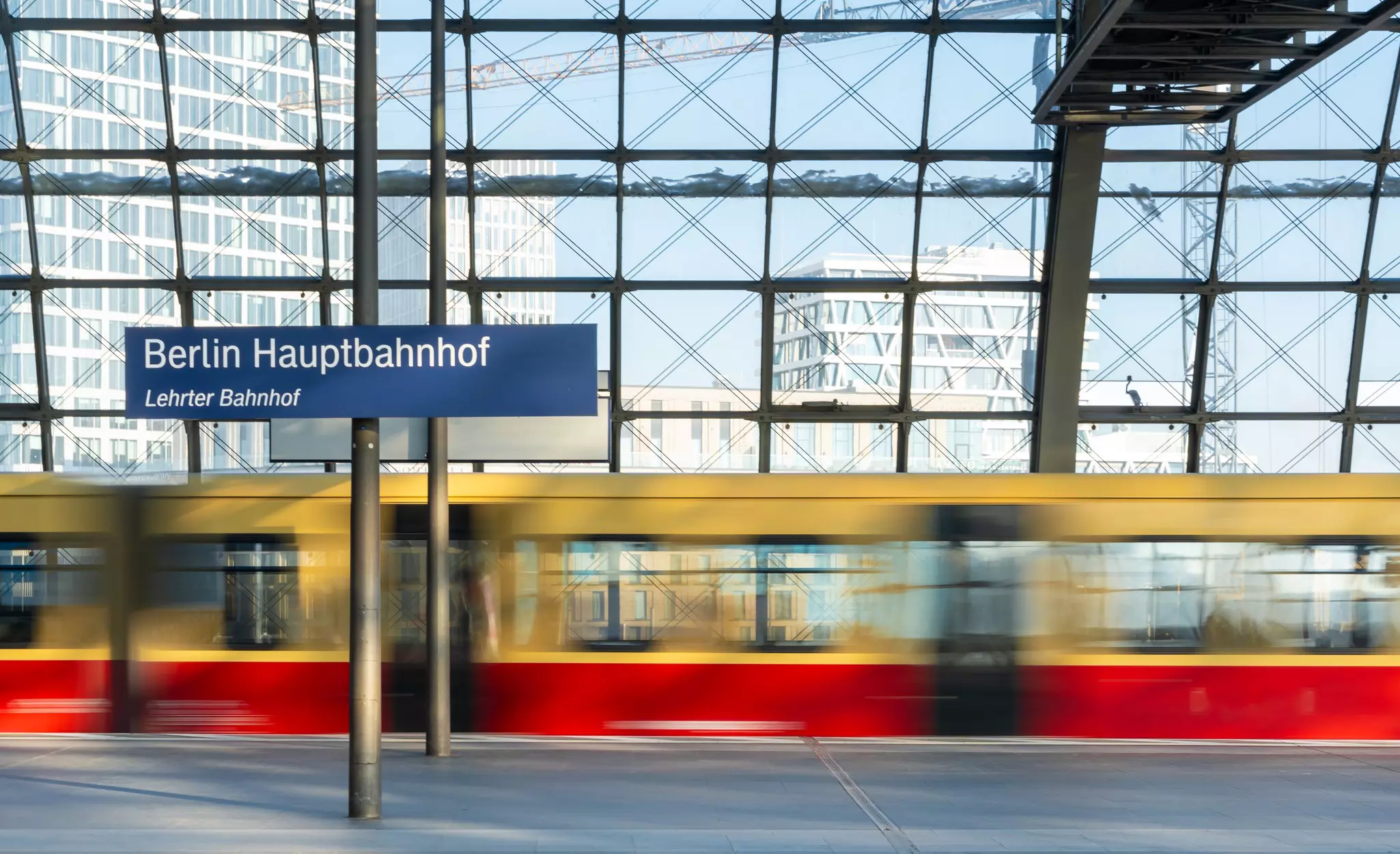 A yellow and red train passes through a station as a blur.