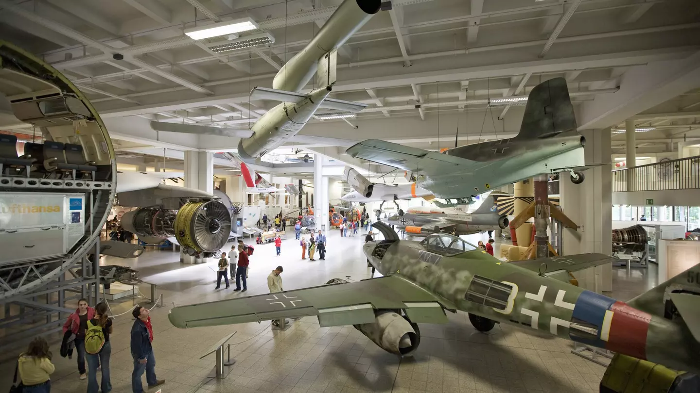 A shot taken from above looking down into a massive museum room furnished with airplanes and other vehicles. People are moving around between the exhibits