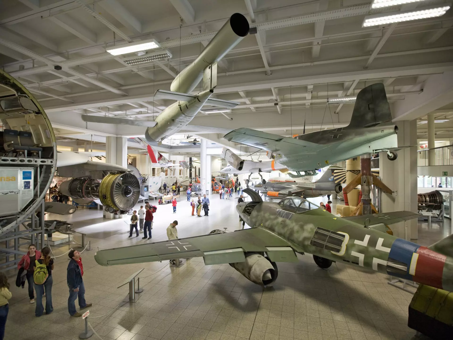 A shot taken from above looking down into a massive museum room furnished with airplanes and other vehicles. People are moving around between the exhibits
