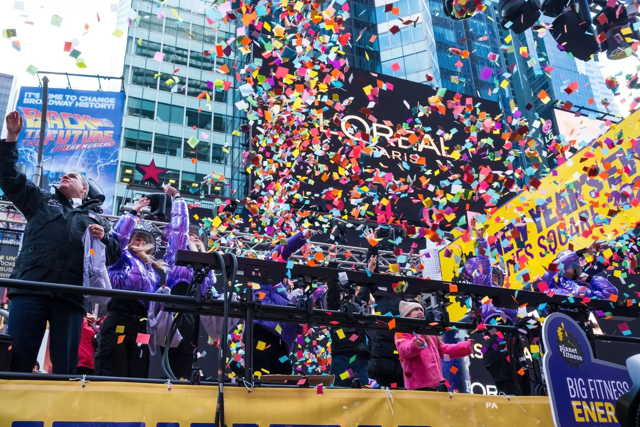 Times Square New Year's Eve celebration with colorful confetti raining over cheering crowds and bright illuminated billboards.