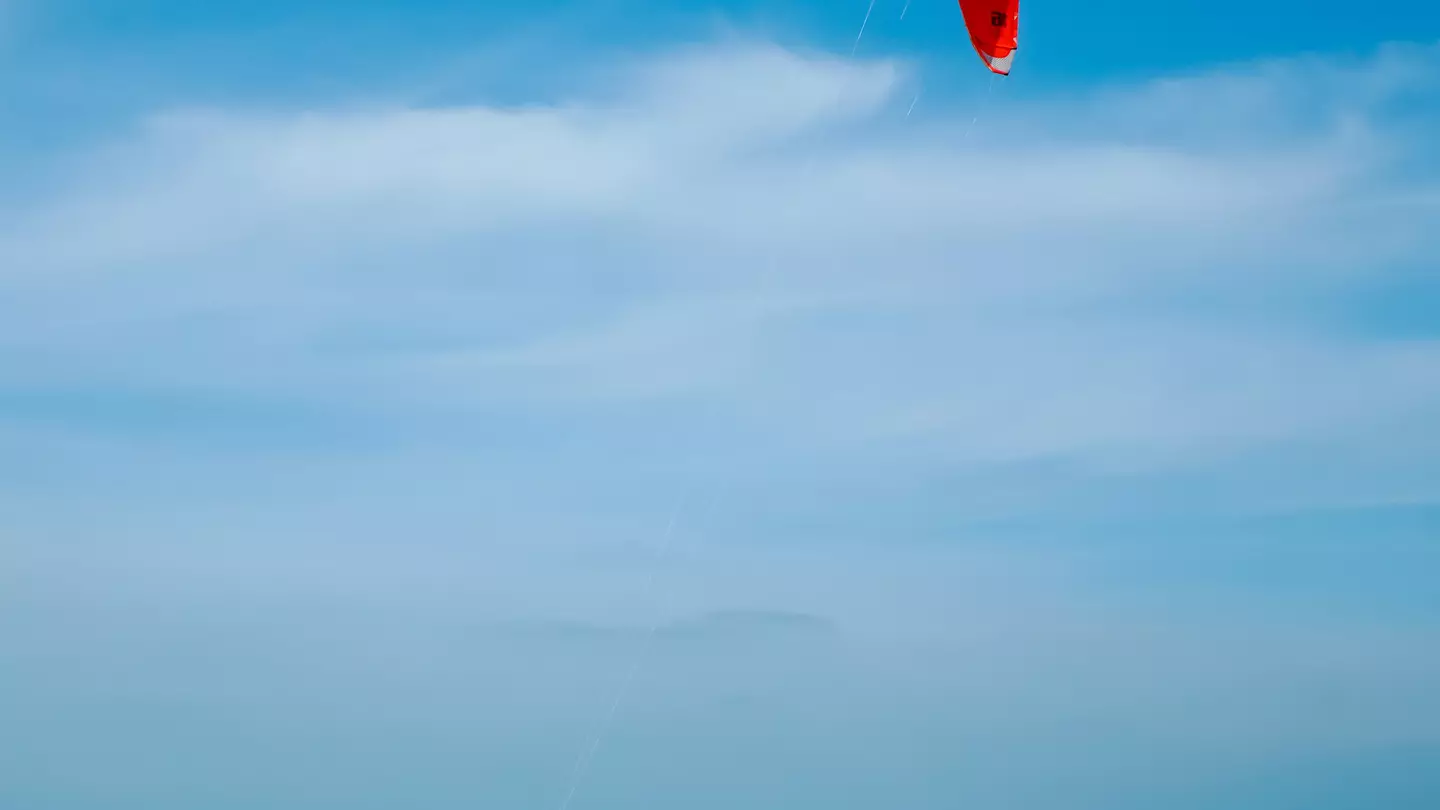 A kitesurfer under a red sail is carried along by the wind on the turquoise waters of Fuwairit Beach, Qatar