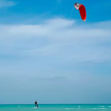 A kitesurfer under a red sail is carried along by the wind on the turquoise waters of Fuwairit Beach, Qatar