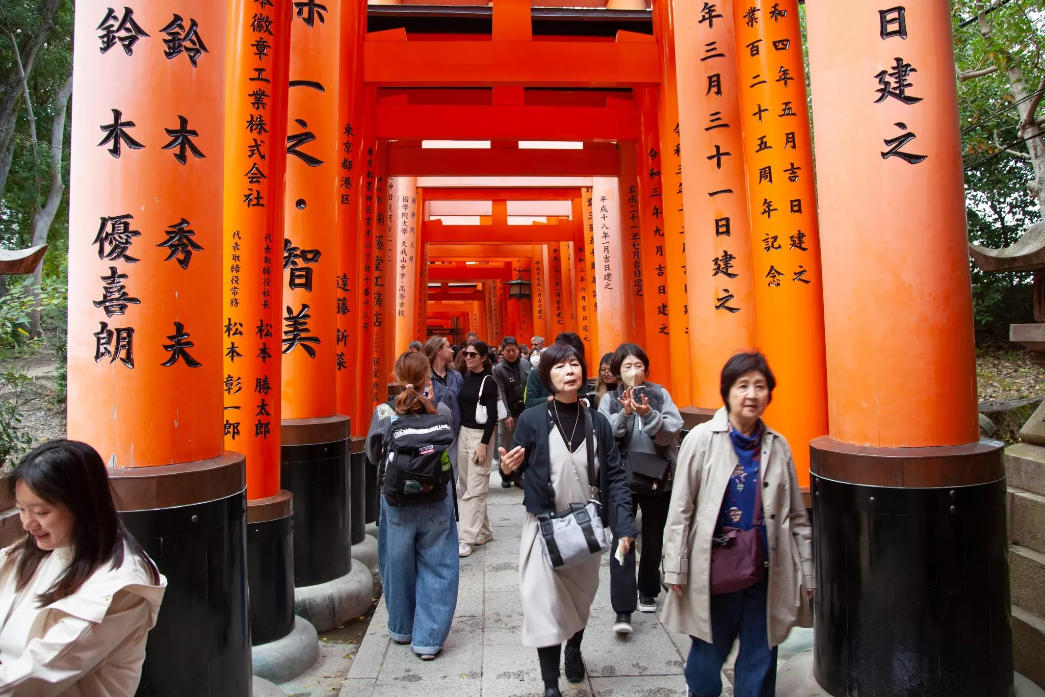People walk through a sequence of bright orange gates painted with characters.