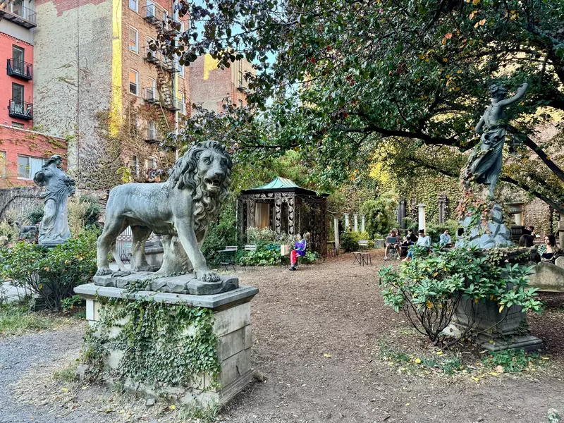 People sitting in a city square with sculptures of human figures and a lion on a sunny, fall day.