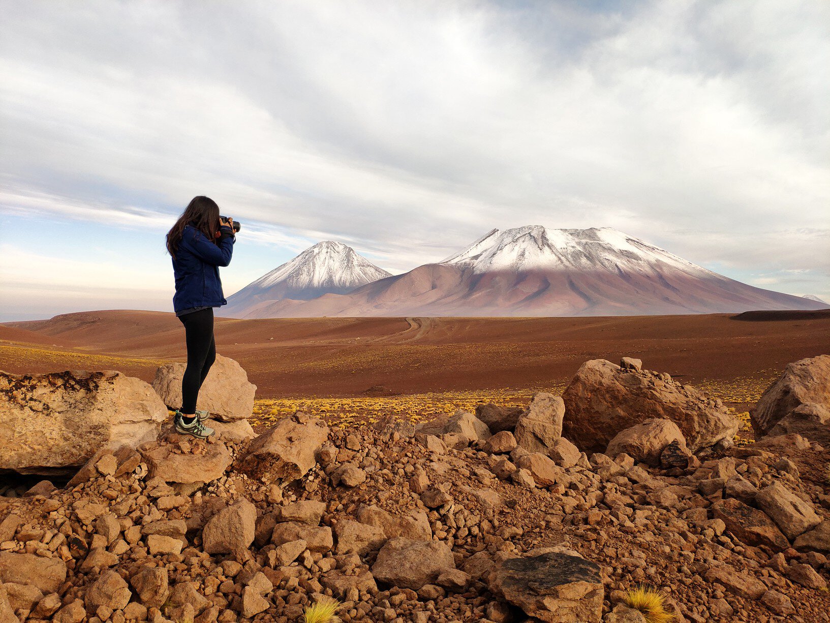 Silhouette of a tourist woman photographing Licancabur and Juriques volcanoes in the border between Chile and Bolivia
